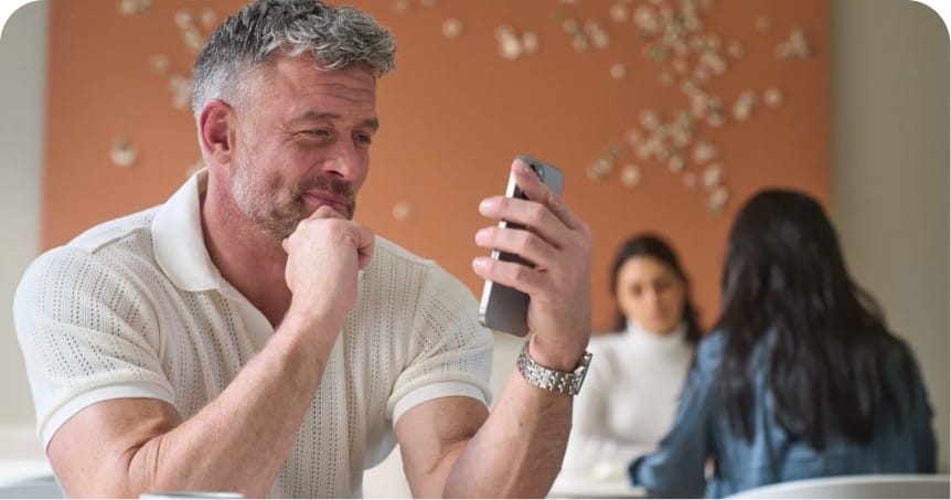 A man sitting at a table inside while looking at his phone.